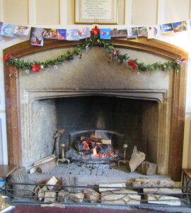 The Common Room fireplace decorated for Christmas with cards hung above and a fire glowing in the grate.